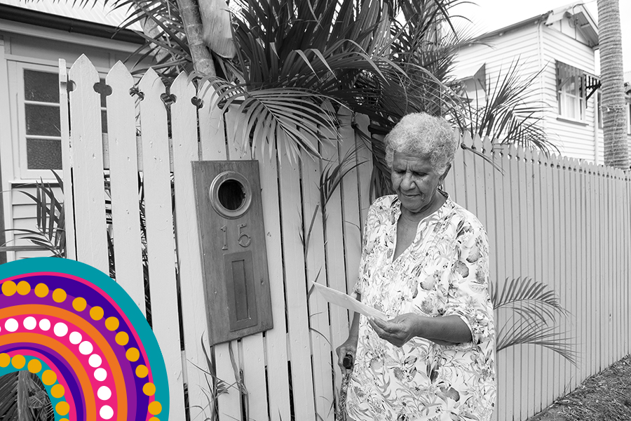 An Aboriginal and Torres Strait Islander woman standing at the letter box, looking at a piece of mail