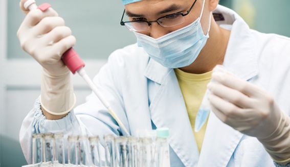 Researcher with face mask uses pipette with test tubes
