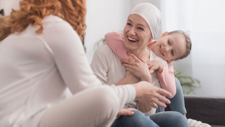 Woman with a headscarf smiles at another woman while a child hugs her