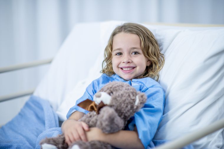 child in bed with teddy smiling
