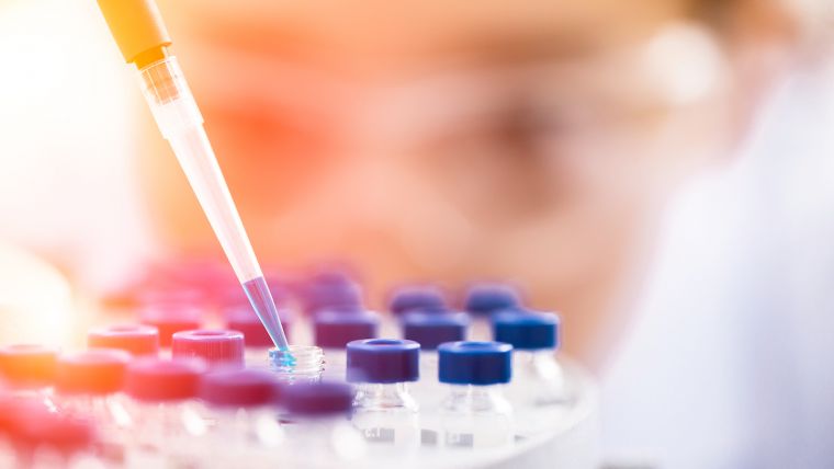Photo is of a researcher dropping blue liquid into a tube.