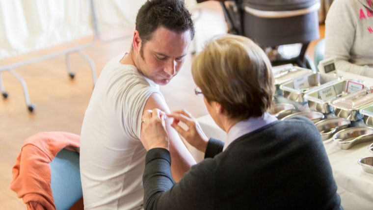 An adult male receiving a vaccination from a nurse.