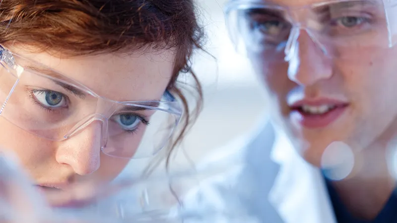 Close up of scientists wearing lab glasses looking at something closely