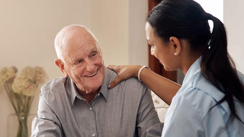 Aged care worker with her hand on the shoulder of a smiling old man