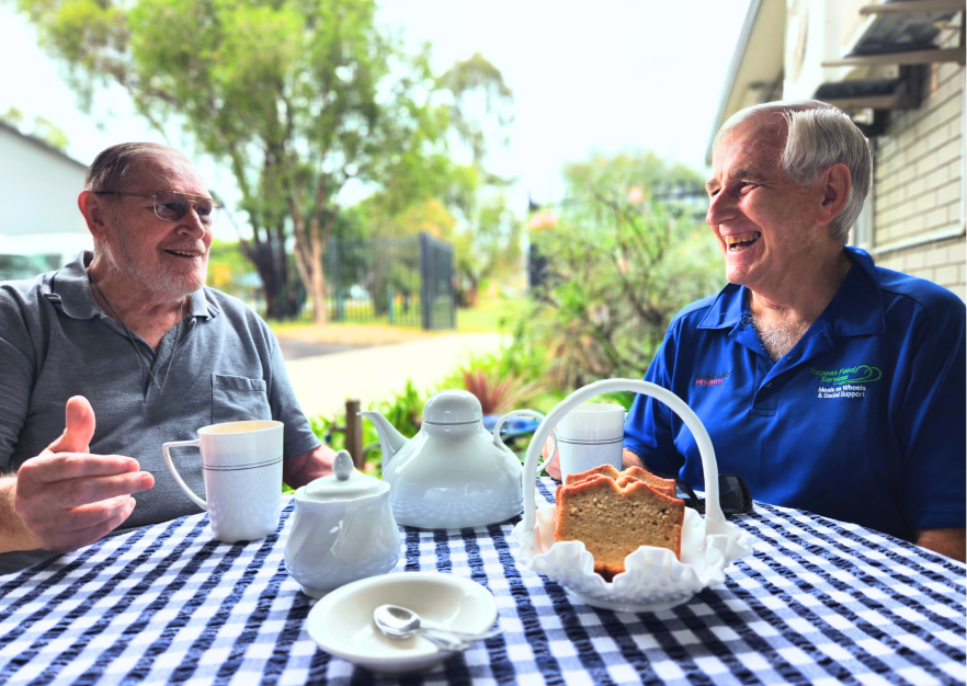 Image of 2 older men chatting and smiling over a cup of tea