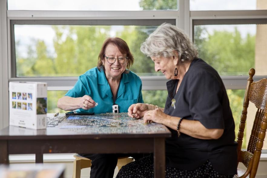 Image of nursing staff and elderly person doing a puzzle.
