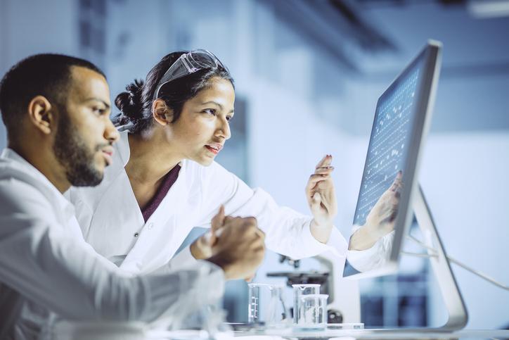 2 people in lab coats looking at a computer