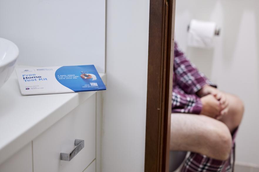 Image of a person sitting on a toilet with the Bowel testing kit in view.