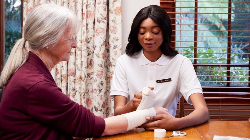 Elderly lady getting her hand bandaged by an aged care nurse