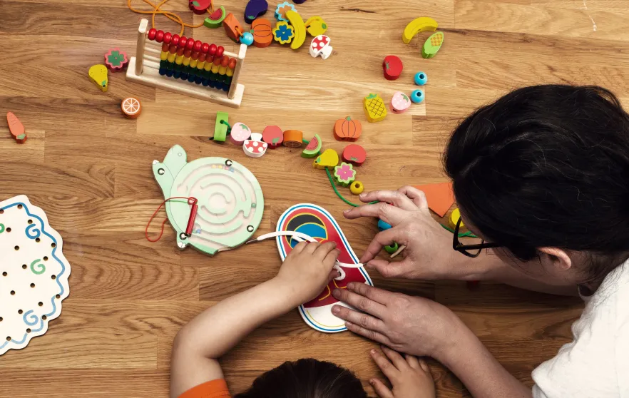A child and early childhood educator playing with toys at a table