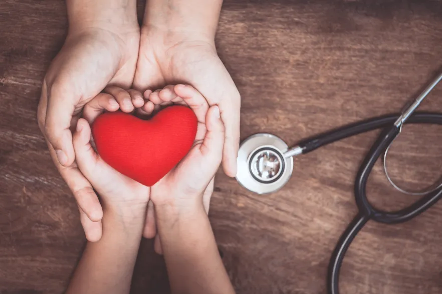 Embraced adult and child hands holding a red heart