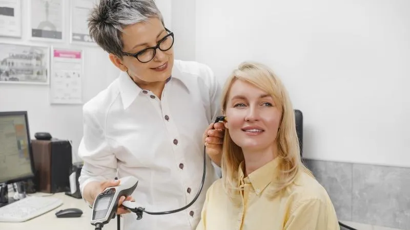 Doctor examining a woman's ear with a testing device in a doctor's office