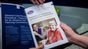 Hands hold open a pamphlet that is displaying information about advance care planning procedures and preparing for an advance care planning conversation.