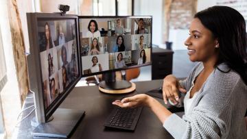 Woman at desk in front of two screens participating in a webinar