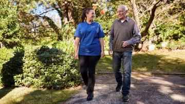 Aged care worker walking beside an elderly man outside in a garden