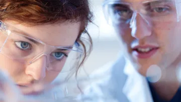 Close up of scientists wearing lab glasses looking at something closely