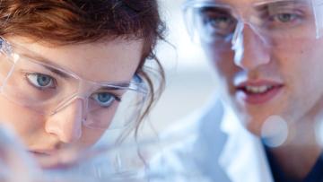 Close up of scientists wearing lab glasses looking at something closely