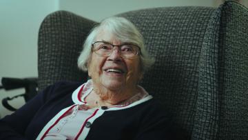 older woman smiling sitting armchair.