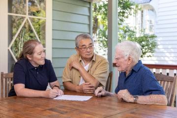 3 people outside on a deck discussing paperwork.