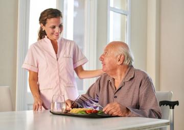 An aged care worker smiles at a senior man who is eating a meal