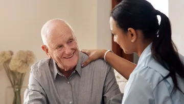 Aged care worker with her hand on the shoulder of a smiling old man
