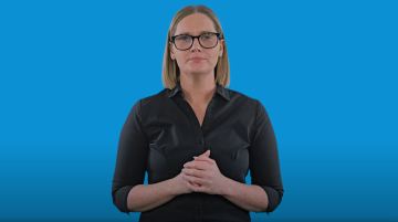 A female Auslan interpreter standing in front of a blue background. 