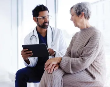 Image of a GP in a white coat sitting with elderly client discussing matters.
