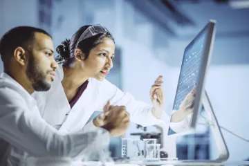 2 people in lab coats looking at a computer