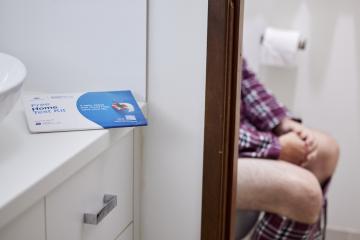 Image of a person sitting on a toilet with the Bowel testing kit in view.