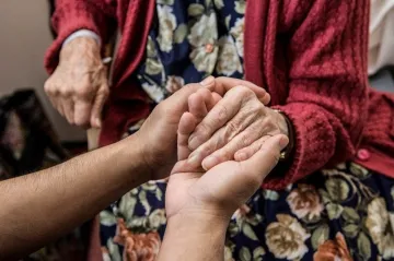 An aged care worker holds the hand of an older person.