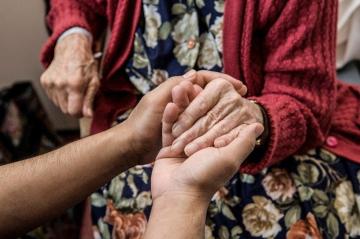 An aged care worker holds the hand of an older person.