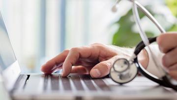 Close up of a laptop keyboard with someone holding a stethoscope