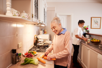 Image of an older woman and a younger female support worker prepare food together in a kitchen.