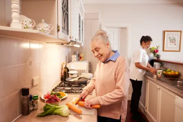 Image of an older woman and a younger female support worker prepare food together in a kitchen.