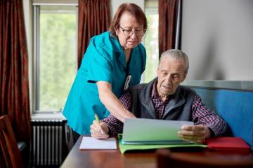 An older man and an aged care worker look at paperwork. 