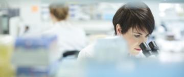 Female lab technician looking through microscope