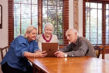 Three elderly people look at a laptop