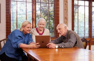 3 people at a dining table looking at a tablet together