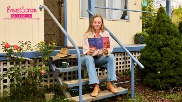 Female sitting on the front stairs of a house reading a BreastScreen Australia flyer