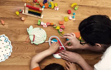 A child and early childhood educator playing with toys at a table