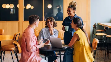 3 people at a coffee table discussing matters with laptop