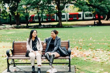 two_young_ethic_women_sitting_and_talking_on_a_park_bench