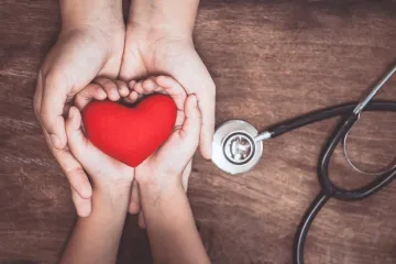 Embraced adult and child hands holding a red heart