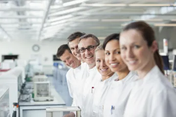 Laboratory staff in white coats smile for the camera