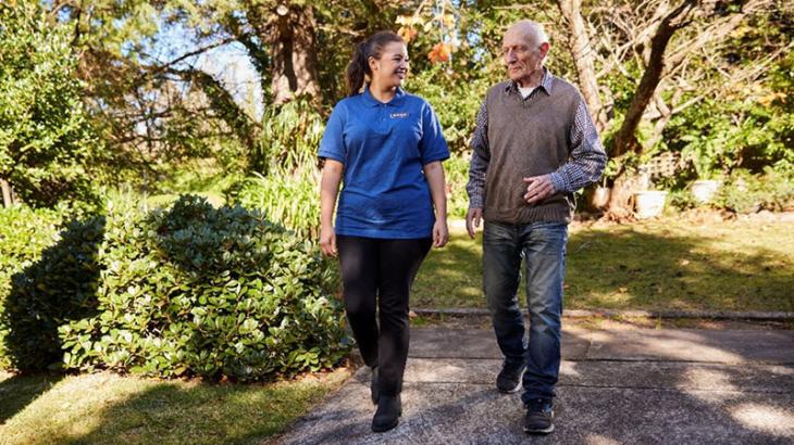 Aged care worker walking beside an elderly man outside in a garden
