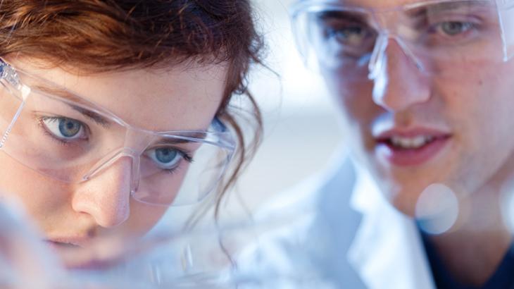Close up of scientists wearing lab glasses looking at something closely