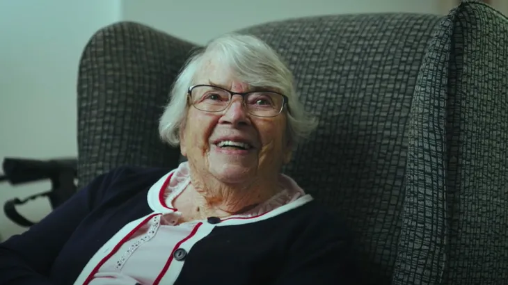 older woman smiling sitting armchair.