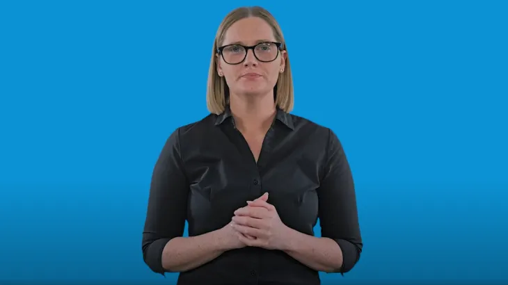 A female Auslan interpreter standing in front of a blue background. 