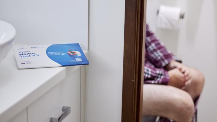 Image of a person sitting on a toilet with the Bowel testing kit in view.