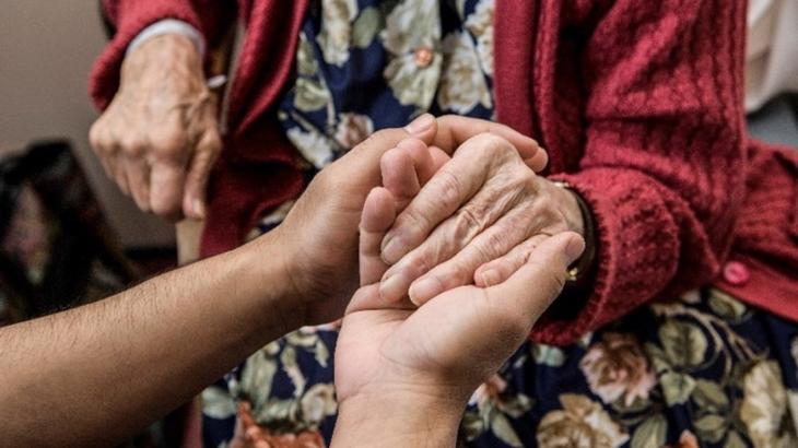 An aged care worker holds the hand of an older person.